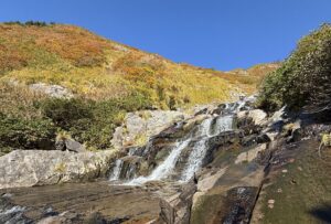 紅葉した山の斜面と、岩の上を流れ落ちる沢